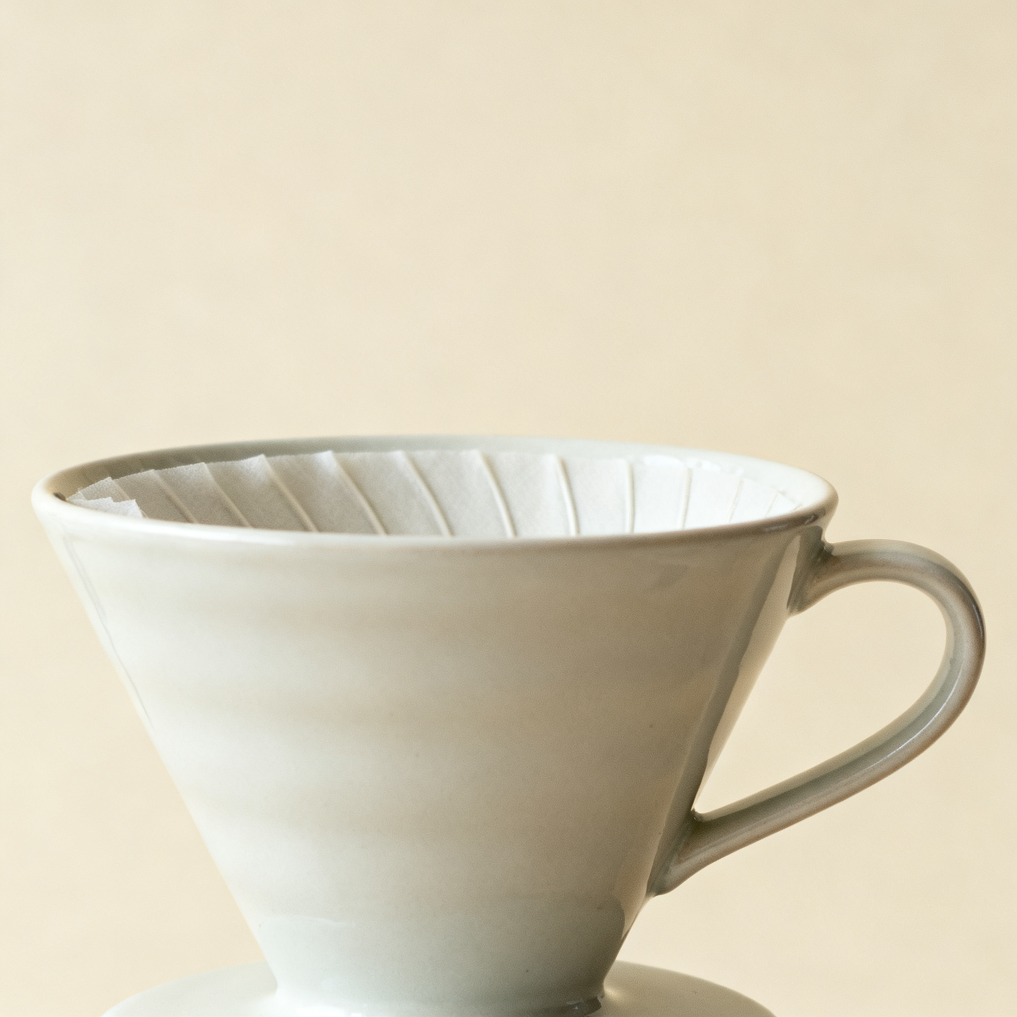 Source product photo: a ceramic pour-over coffee dripper on a plain cream backdrop, used as the starting image for the video generation examples below