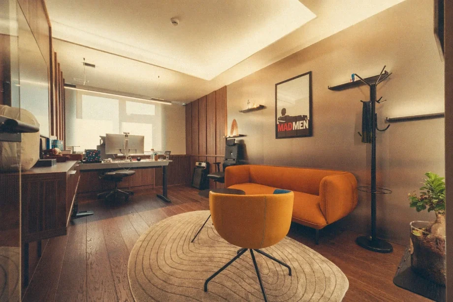 Private office with wooden desk, orange sofa, yellow swivel chair, and Mad Men poster at Coinis HQ