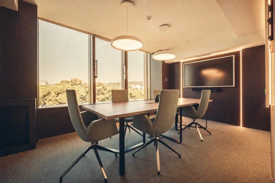Top-floor meeting room with four beige chairs, wall-mounted screen, and tree-line view at Coinis HQ