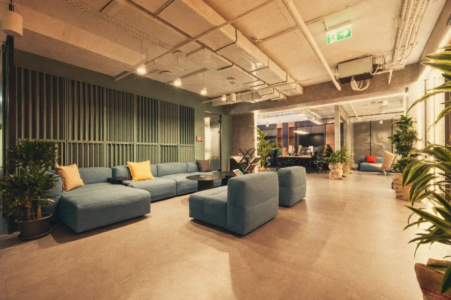 Large common lounge with blue modular sofas against a green louvered wall at Coinis HQ