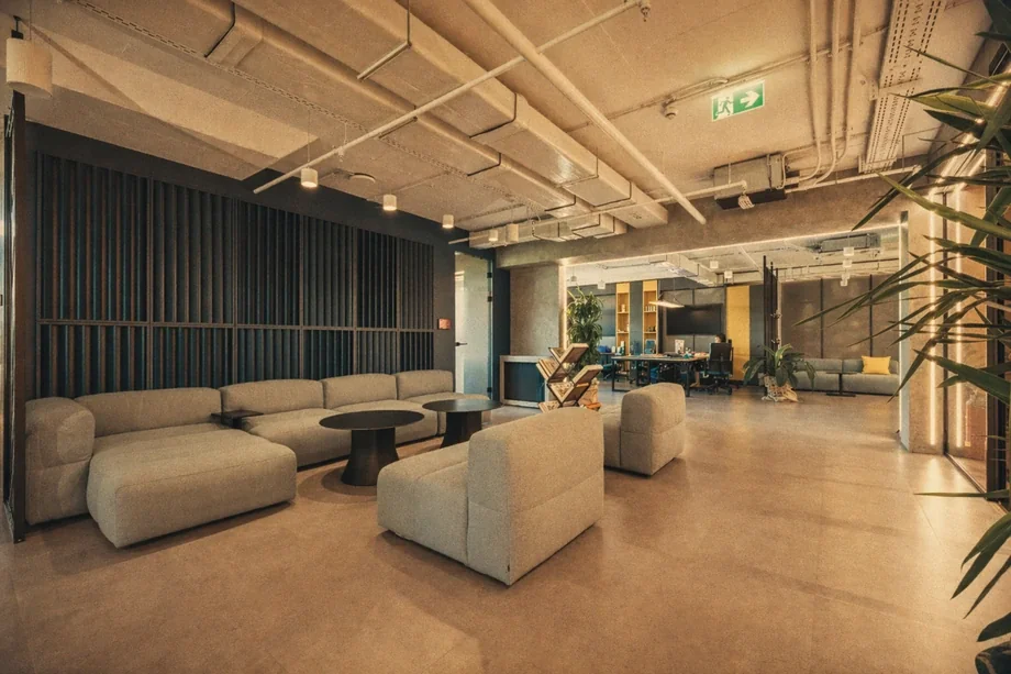 Open lounge with grey modular sofas, black louvered accent wall, and concrete pillars at Coinis HQ