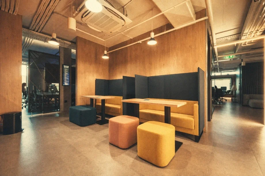 Cafe booth seating with yellow banquettes and colored poufs against a wood-paneled wall at Coinis HQ