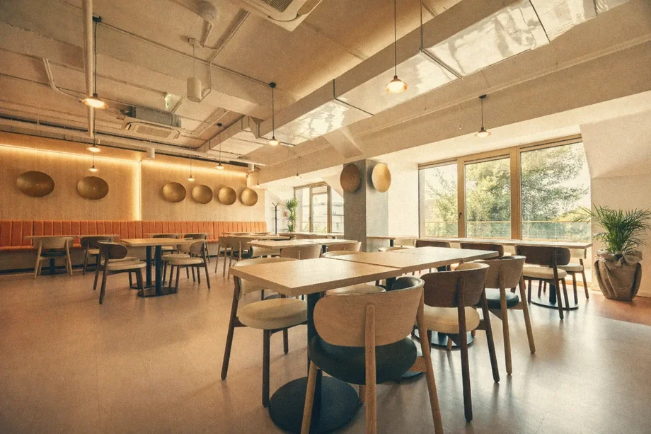 Office canteen with wooden tables, orange banquette, and pendant lights at Coinis HQ