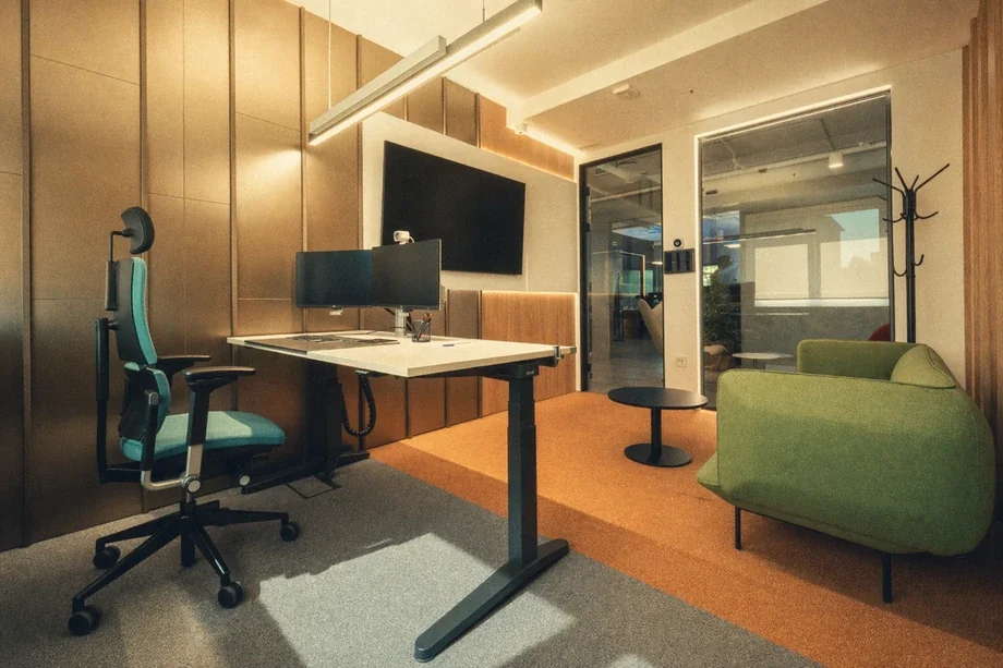 Private focus office with standing desk, curved dual monitor, teal chair, and green sofa at Coinis HQ