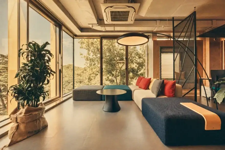 Lounge with modular sofa in front of floor-to-ceiling windows overlooking tree canopy at Coinis HQ