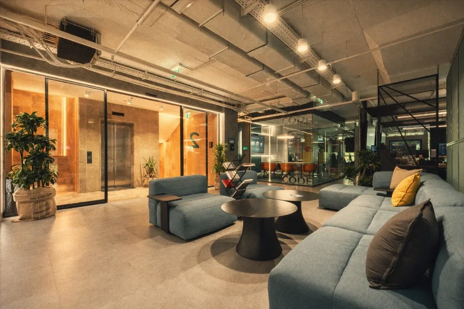 Lobby lounge with blue modular sofas beside a glass-walled Code meeting room at Coinis HQ
