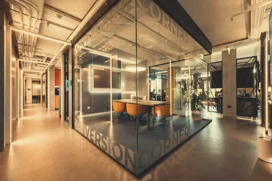 Glass-walled Conversion Corner meeting room with orange chairs and wall display at Coinis HQ