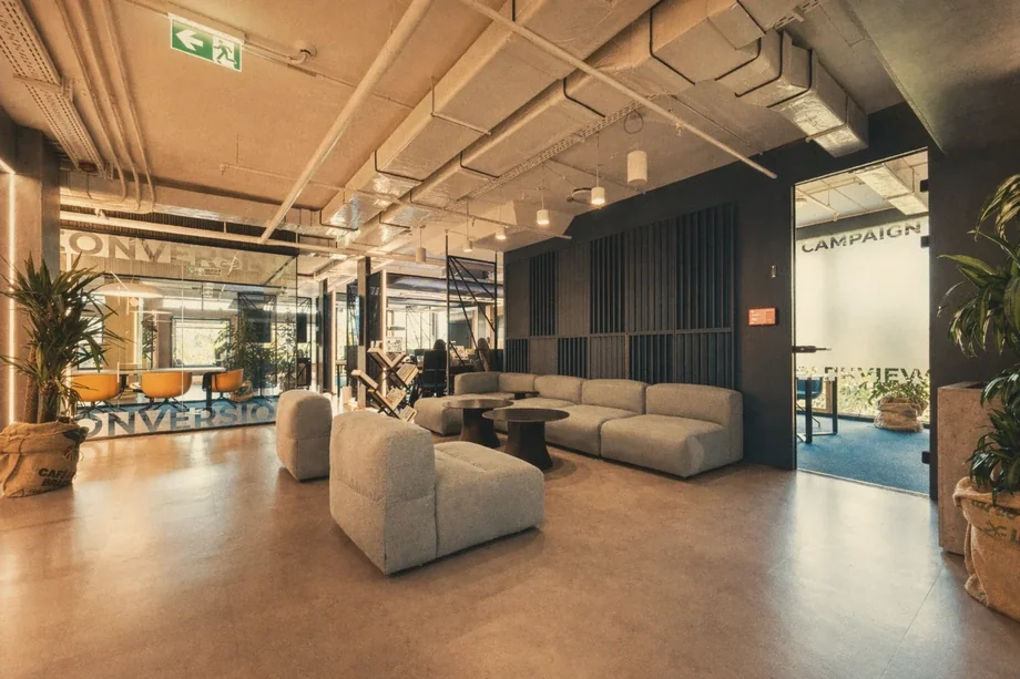 Common area with grey boucle sofas between glass Campaign and Conversion meeting rooms at Coinis HQ