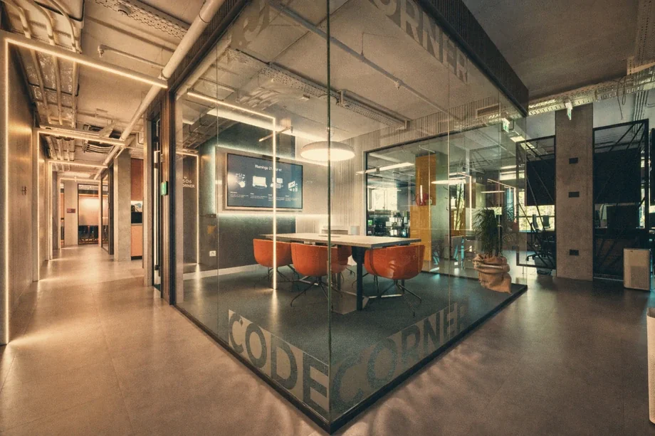 Glass-walled meeting room labeled Code Corner with orange chairs and wall display at Coinis HQ